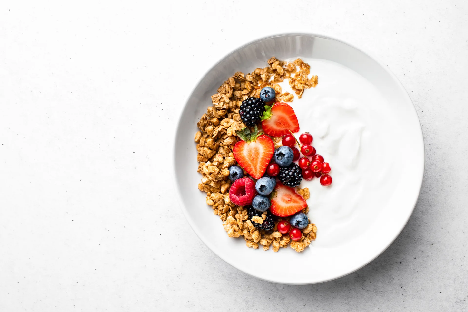 A small serving of natural yoghurt with granola and berries on a wide white plate